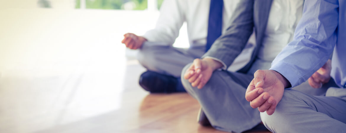 The lower bodies of three men in suits sitting down cross-legged in a meditation position.