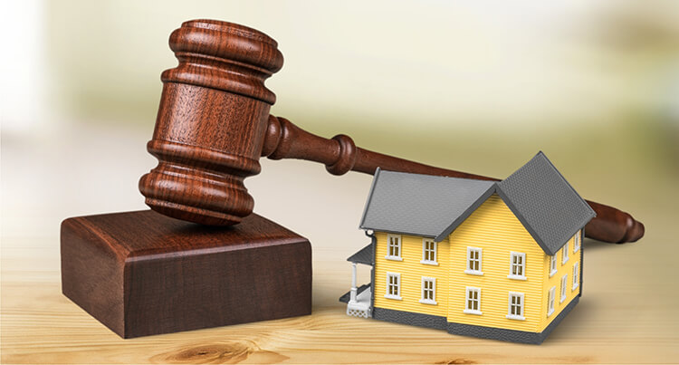 A brown wooden gavel and small toy house next to one another on a table