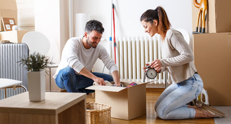 A middle-aged man and a brown-haired woman in jeans and a cream sweater holds a clock as they pack a box in their living room at home