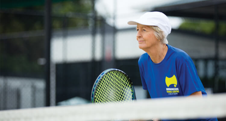 A lady playing tennis who is positioned at the net and waiting to volley the ball