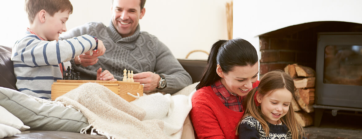 Family playing games together in living room and in front of fireplace.